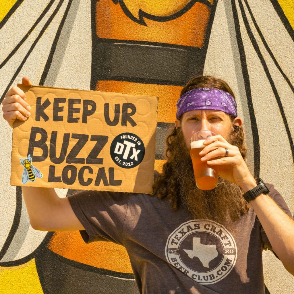 Man drinking Local Buzz in Dallas, TX holding a sign that says "Keep your buzz local".