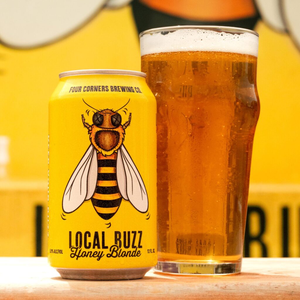 A can of Local Buzz next to a glass of beer in front of the Local Buzz mural at Four Corners Brewing Co. in Dallas, TX.
