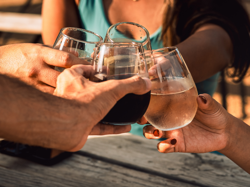 Group of friends clinking stemless glasses of beer outdoors at golden hour