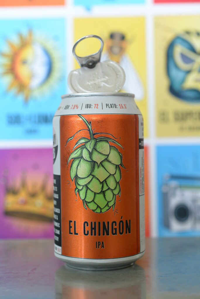 An open Four Corners Brewing Co. El Chingón IPA can with its 360° pop top lid flipped back, displayed against a colorful lotería-style poster backdrop.