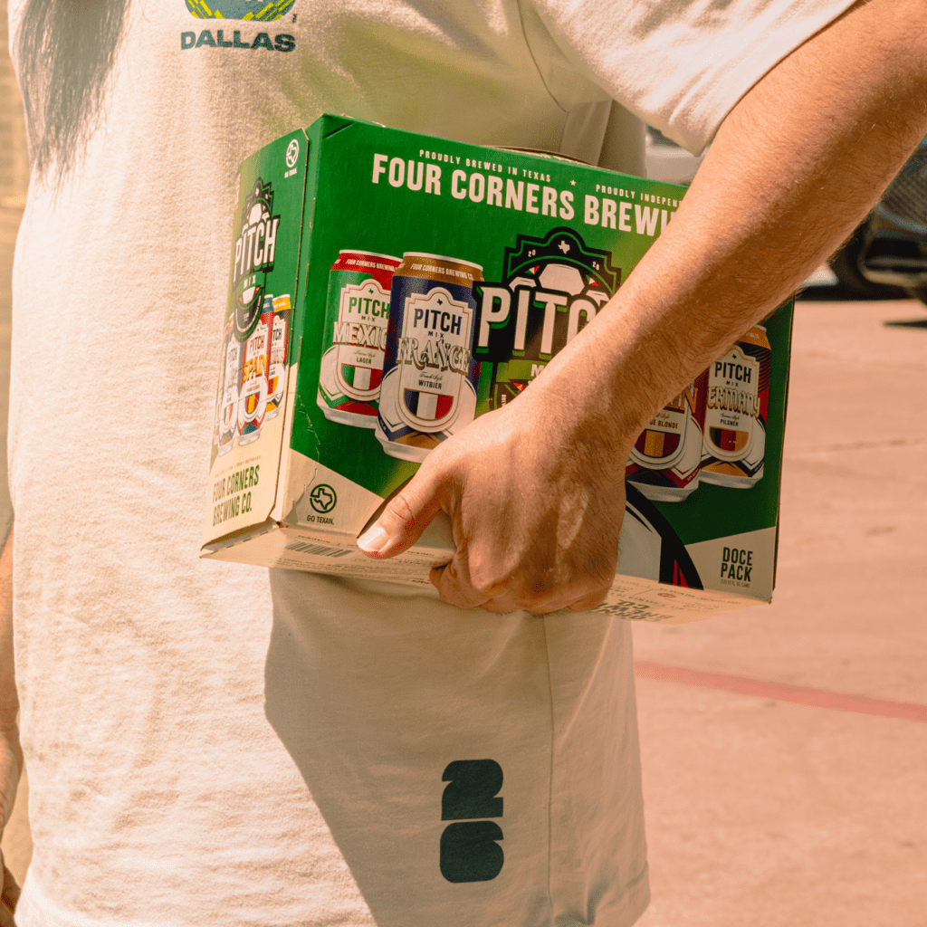 Person in a Dallas shirt carrying a Four Corners Brewing Co. Pitch Mix 12-pack variety box outdoors