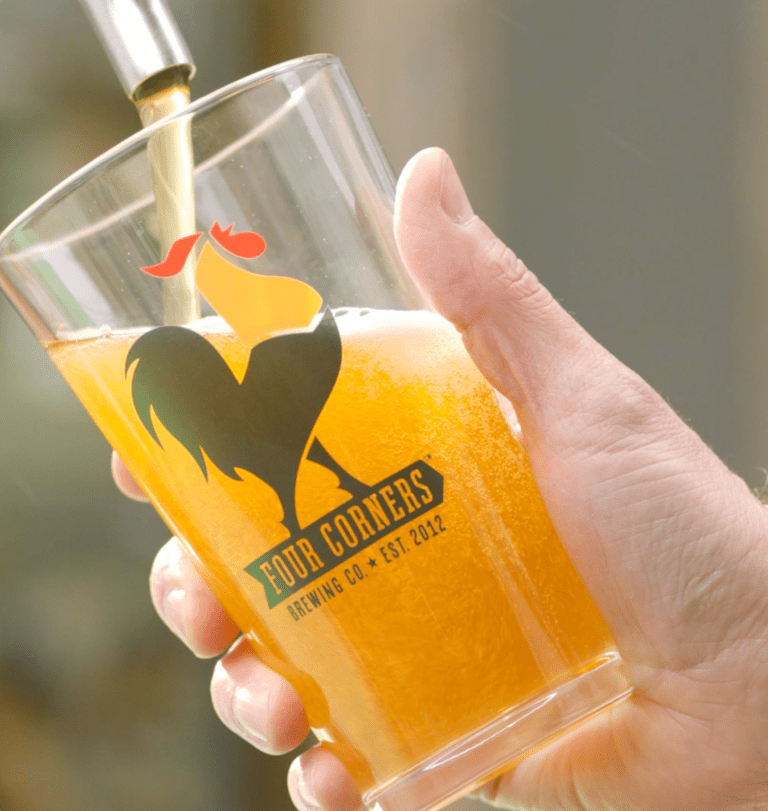 Golden beer being poured from a tap into a Four Corners Brewing Co. branded pint glass held by hand outdoors