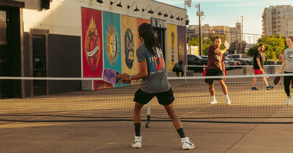 Players competing in pickleball in front of Four Corners Brewing Co.'s colorful taproom murals at golden hour