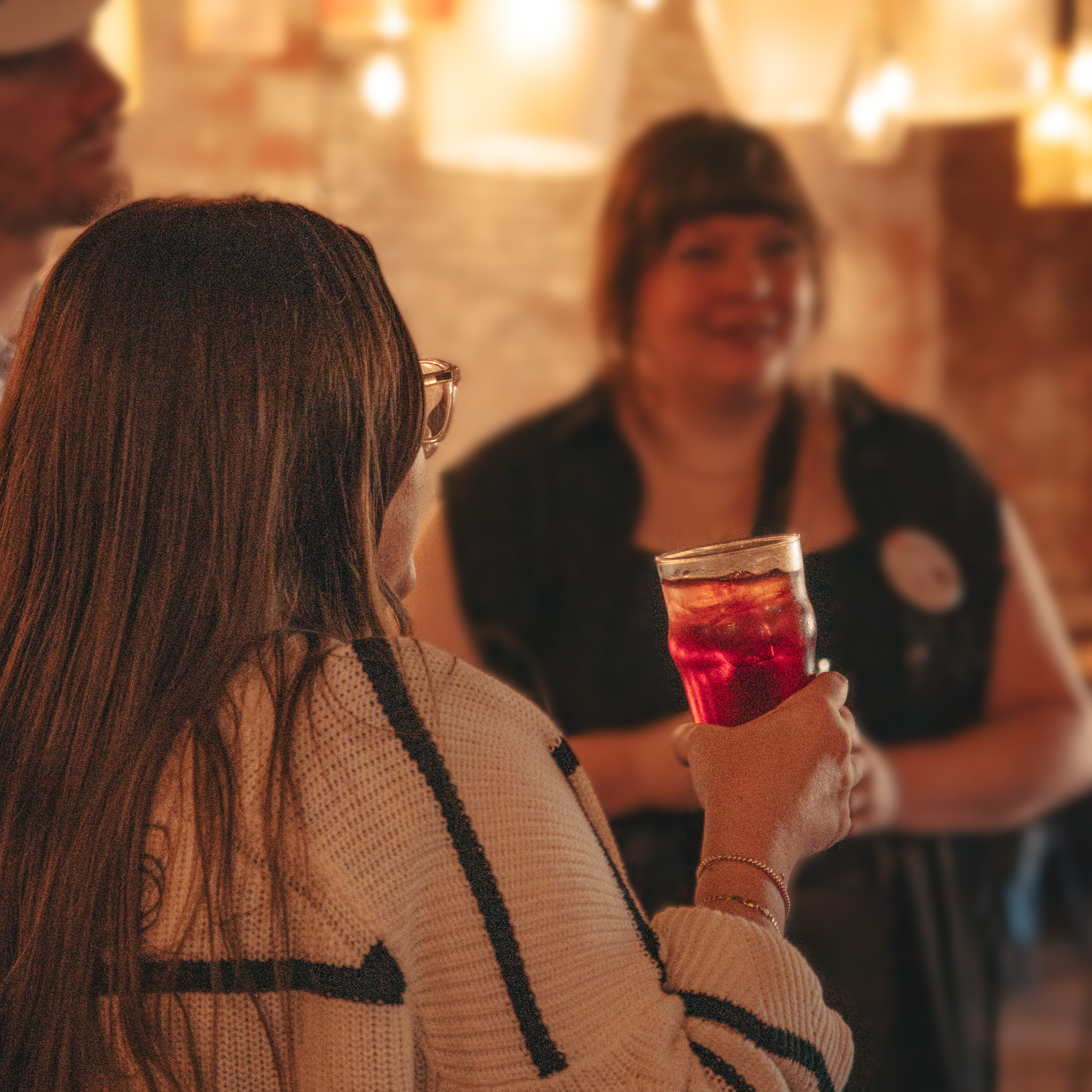 A group of friends chatting inside the Four Corners Brewing Co. Taproom. In focus is a pint of a berry colored cocktail.